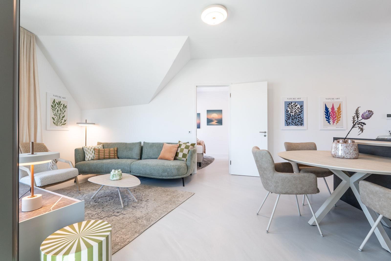 Wohn- und Essbereich mit Sofa, Tisch und Stühlen. Dachschräge und Wandbilder sichtbar.