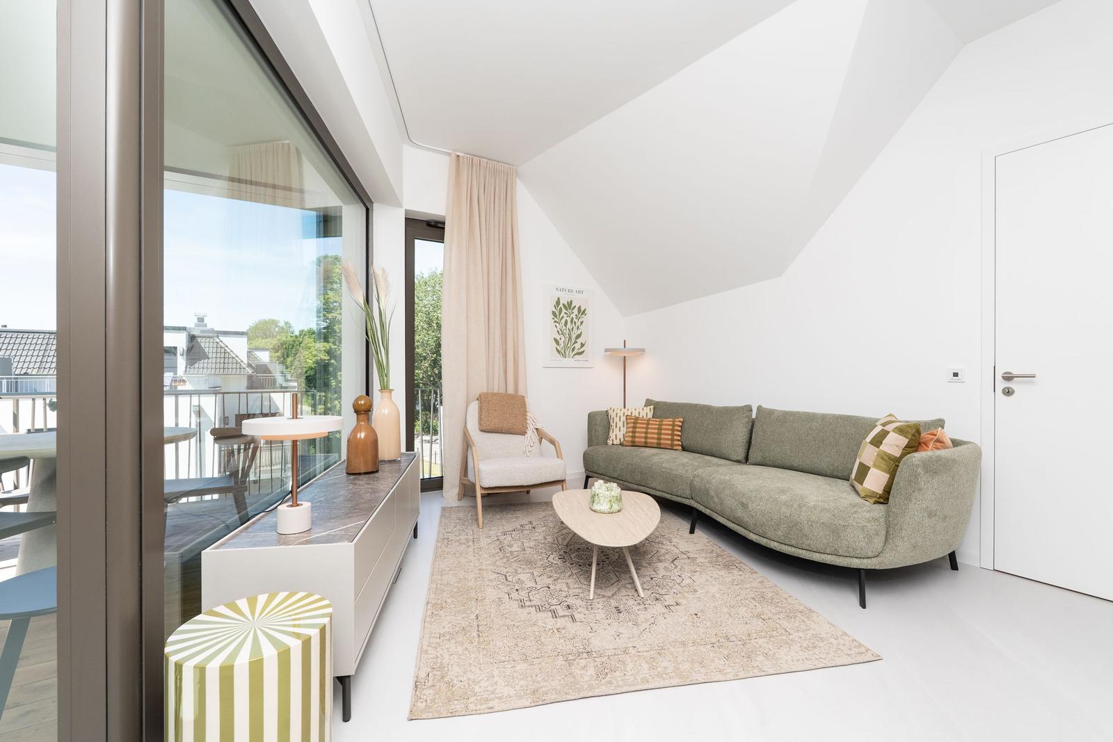 Ein Wohnzimmer mit grünem Sofa, Holztisch und großem Fenster zur Terrasse.