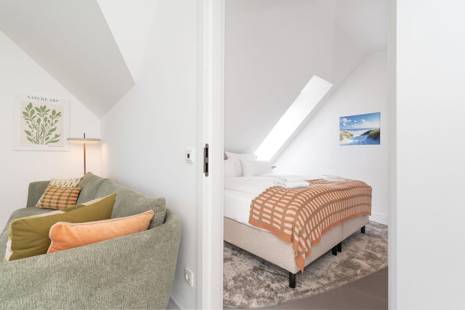 Schlafzimmer mit Dachschräge und großem Fenster. Wohnbereich mit Sofa und Kissen.