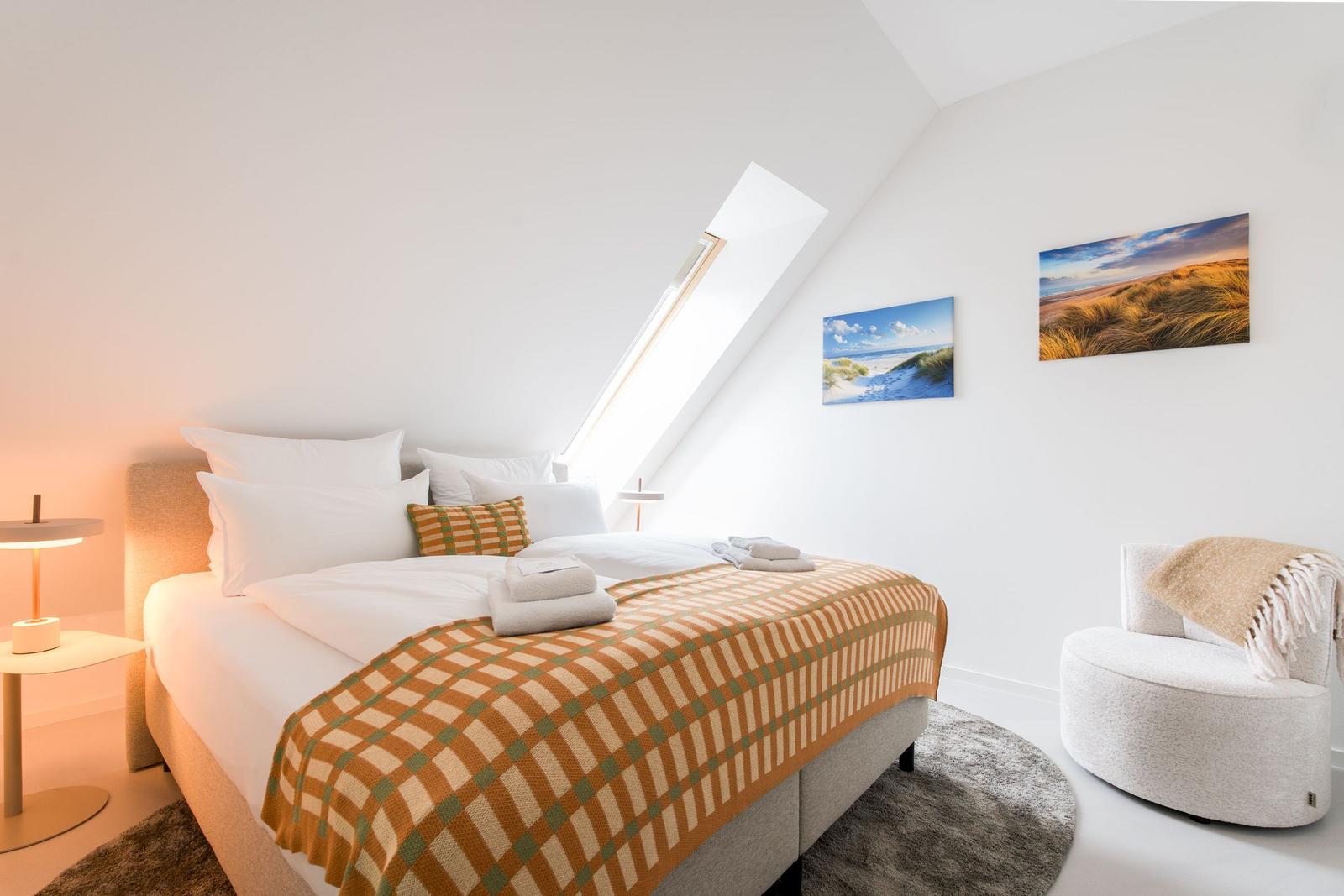Schlafzimmer mit Dachfenster, Bett, Sessel und Wandbildern.