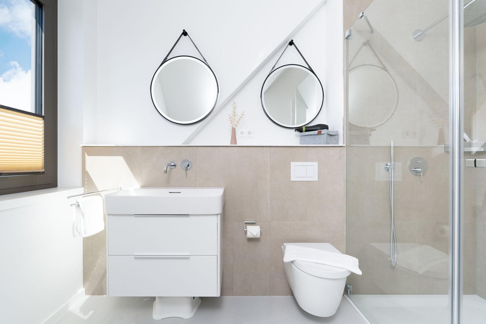 Badezimmer mit Dusche, Waschbecken und Toilette. Zwei runde Spiegel an der Wand.