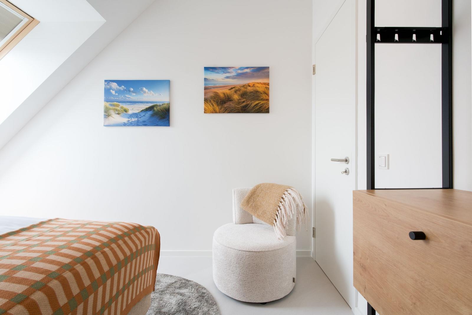 Schlafzimmer mit Dachschräge, Bett, Sessel und Wandbildern.