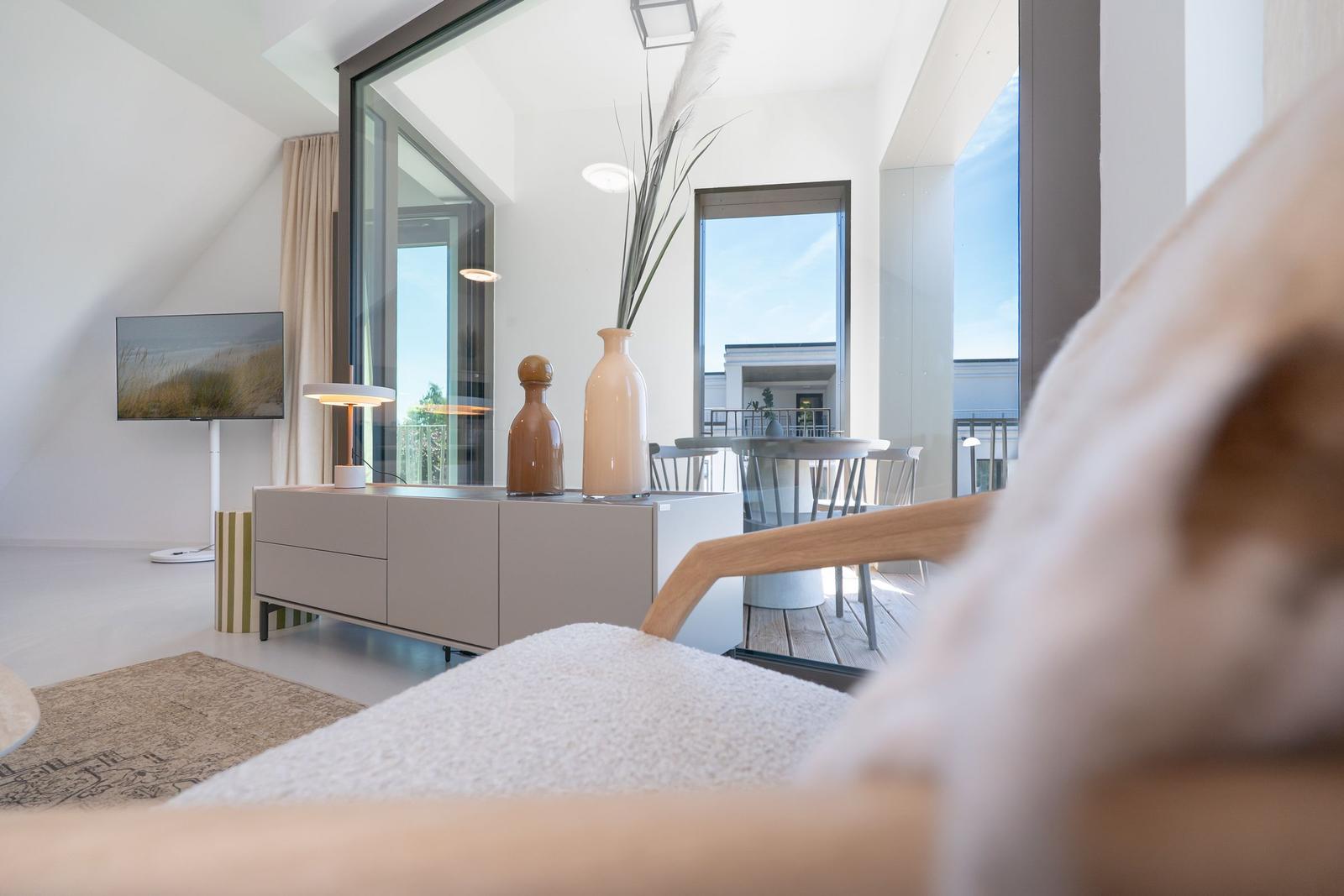 Wohnbereich mit Fernseher, Sideboard und Blick auf Balkon.