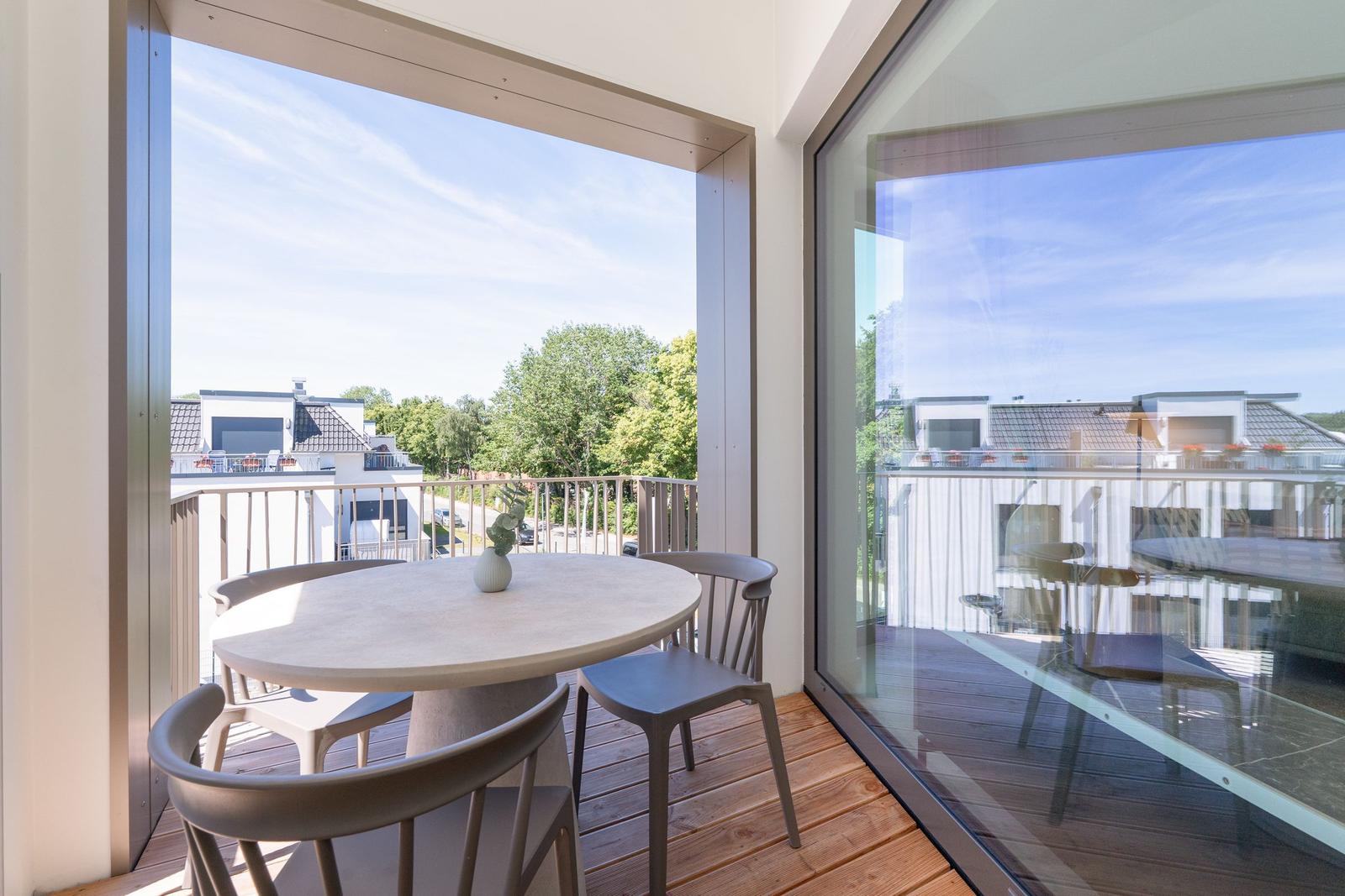 Terrasse mit runden Tisch und Stühlen. Blick auf Wohnhäuser und Bäume.