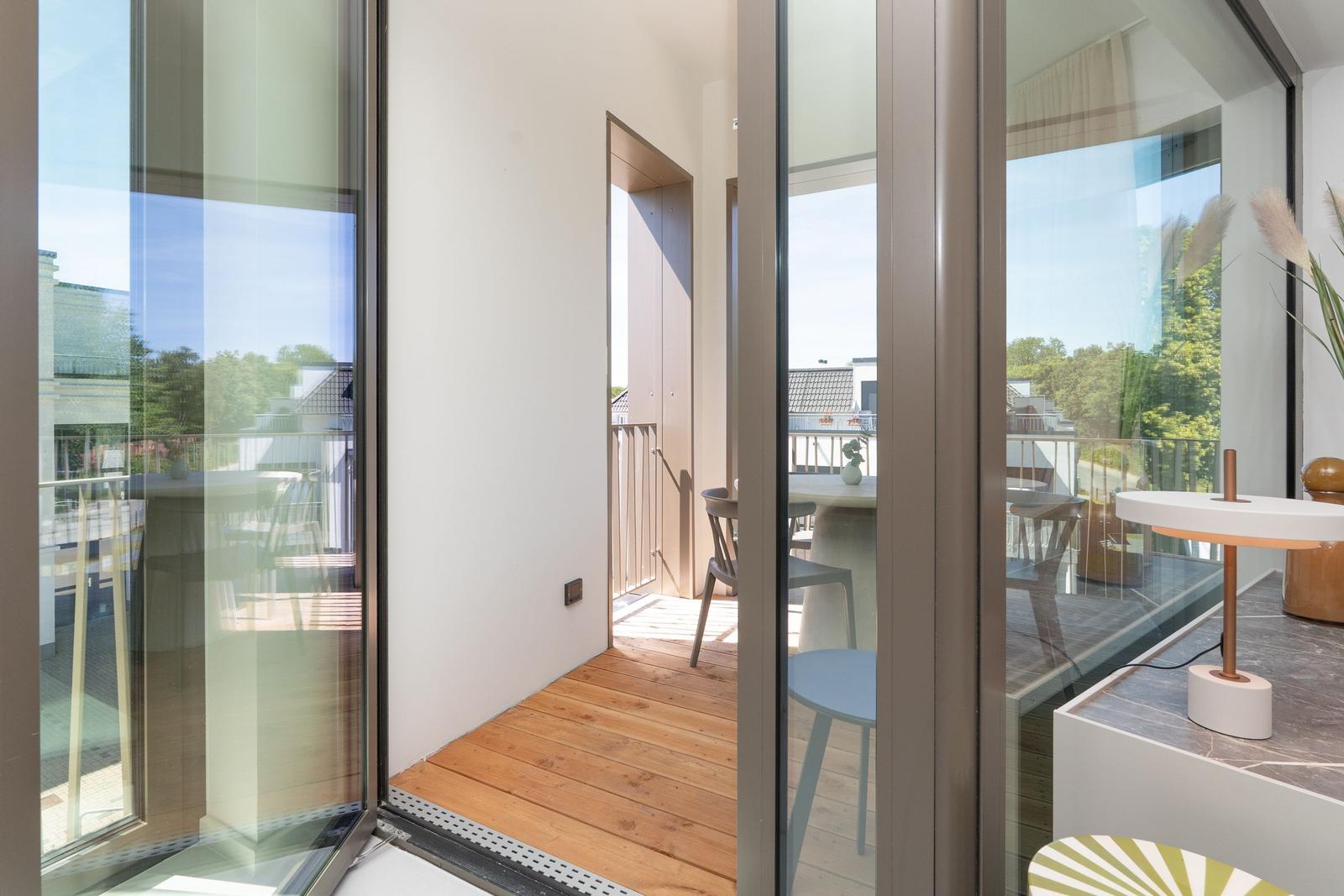 Durchgehende Glasfront öffnet sich zu einer Terrasse mit Holzboden und Gartenblick.