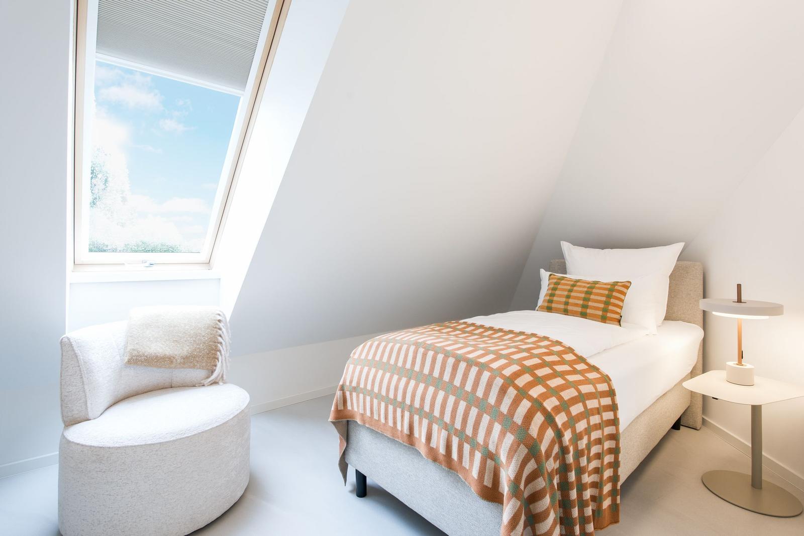 Ein Schlafzimmer mit Dachschrägen, Bett, Sessel und Fenster.