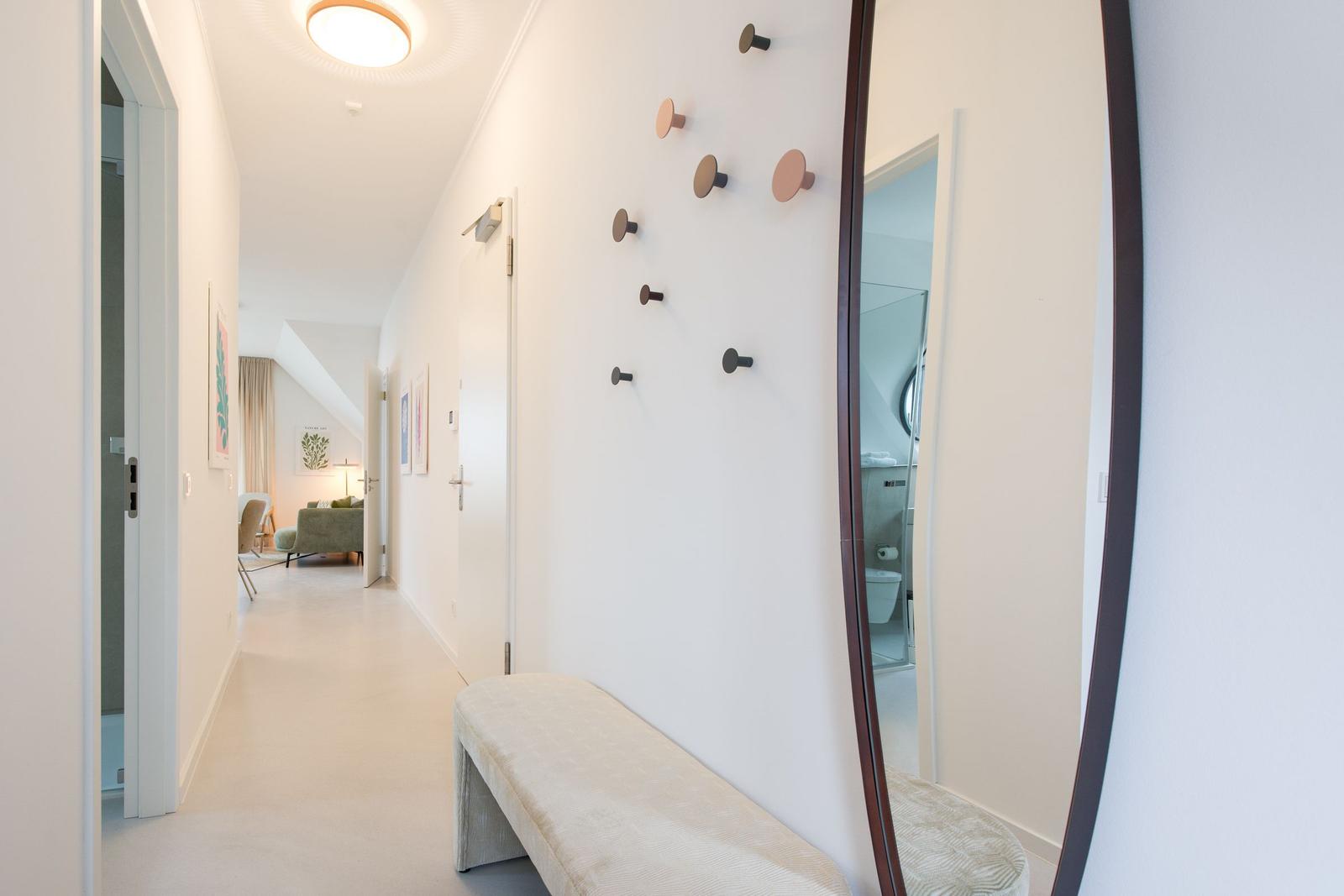 Flur mit Hocker, Wandhalterungen und Blick in Wohn- und Badezimmer.