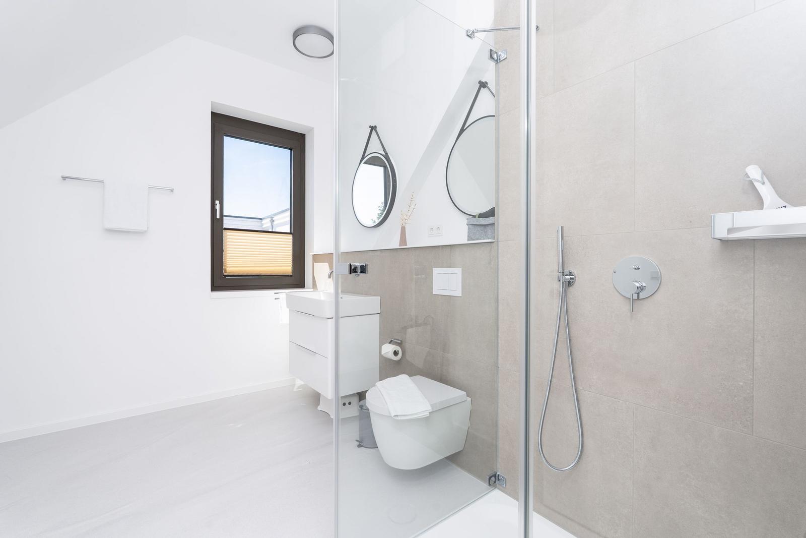 Moderne Dusche mit Glaswand, Waschbecken und Toilette. Fenster mit Jalousie.