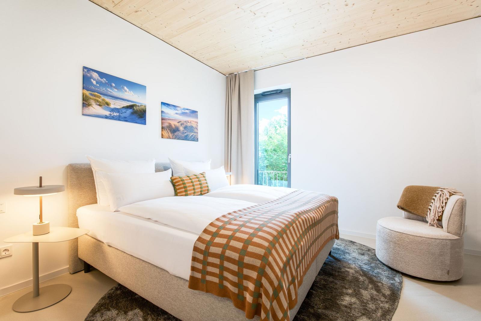 Schlafzimmer mit Bett, Sessel und Fenster zum Balkon.