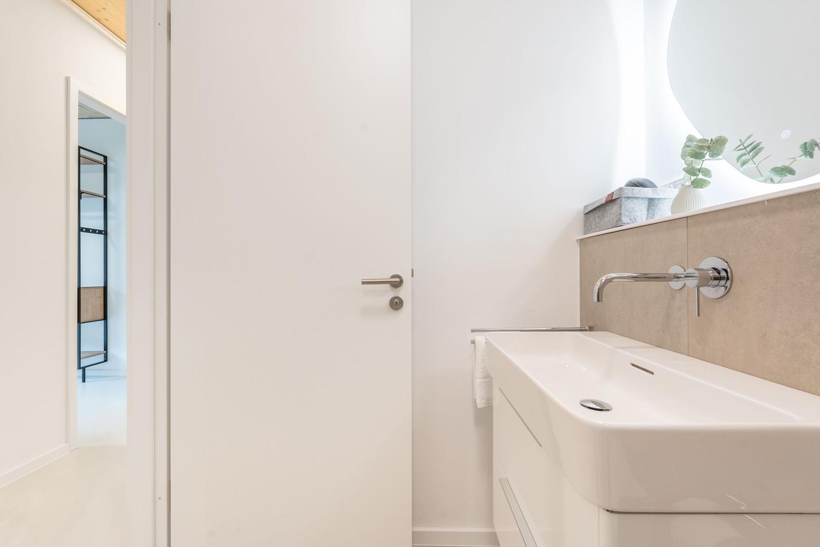 Badezimmer mit Waschbecken, Spiegel und Tür zum Ankleideraum.