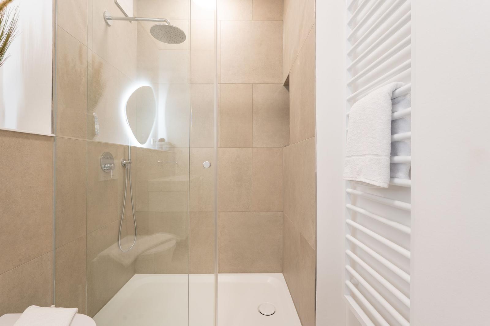 Dusche mit Glaswand, Duschbrause und Heizung. Handtuch auf Heizung.