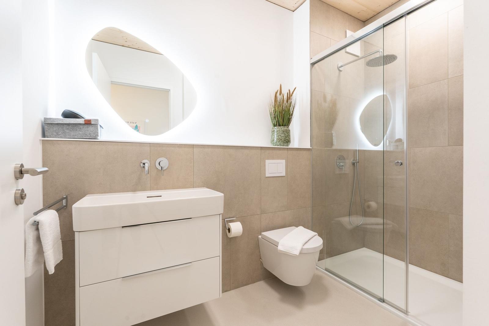 Badezimmer mit Dusche, Waschbecken und Toilette. Moderne Einrichtung und Beleuchtung.