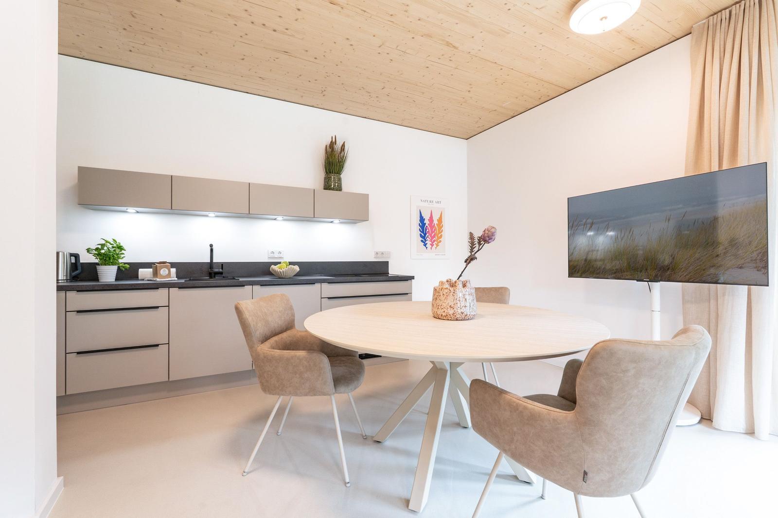 Küche mit Essbereich, runder Tisch und Stühle, Fernseher an der Wand.