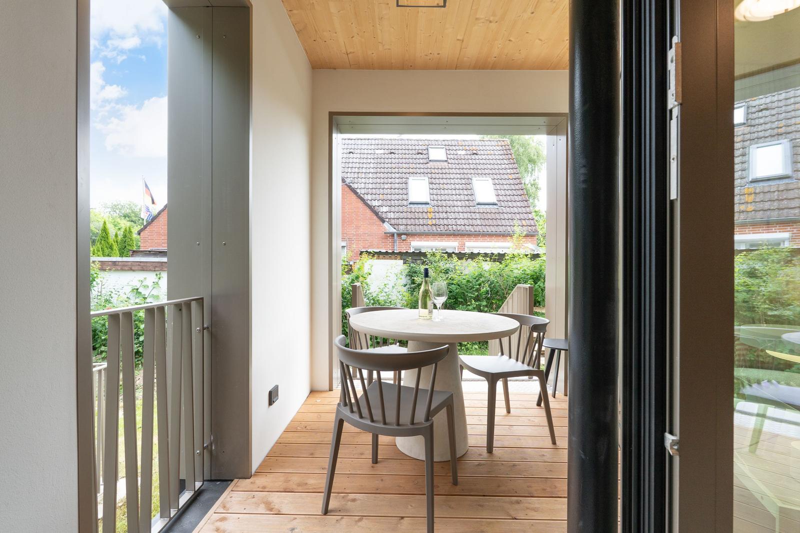 Terrasse mit runden Tisch und Stühlen, Holzboden und Blick auf Garten und Haus.