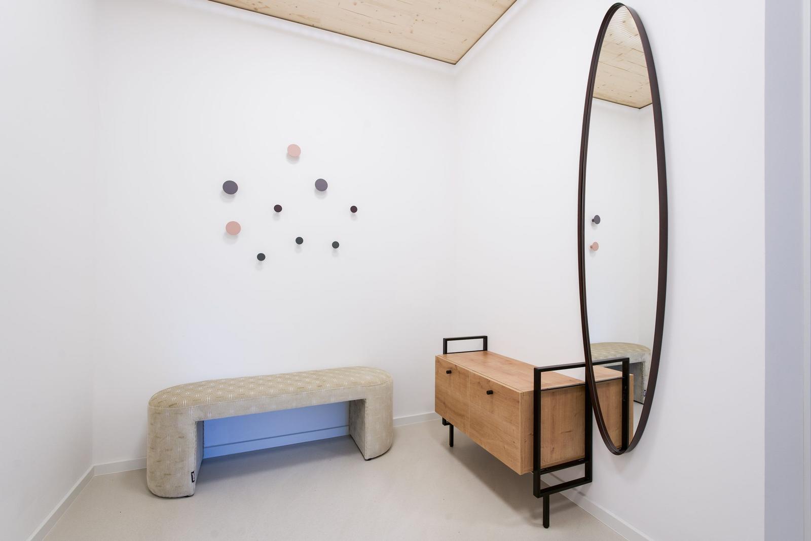 Ein Raum mit Bank, Schrank und Wandspiegel. An der Wand hängt eine runde Kunstinstallation.