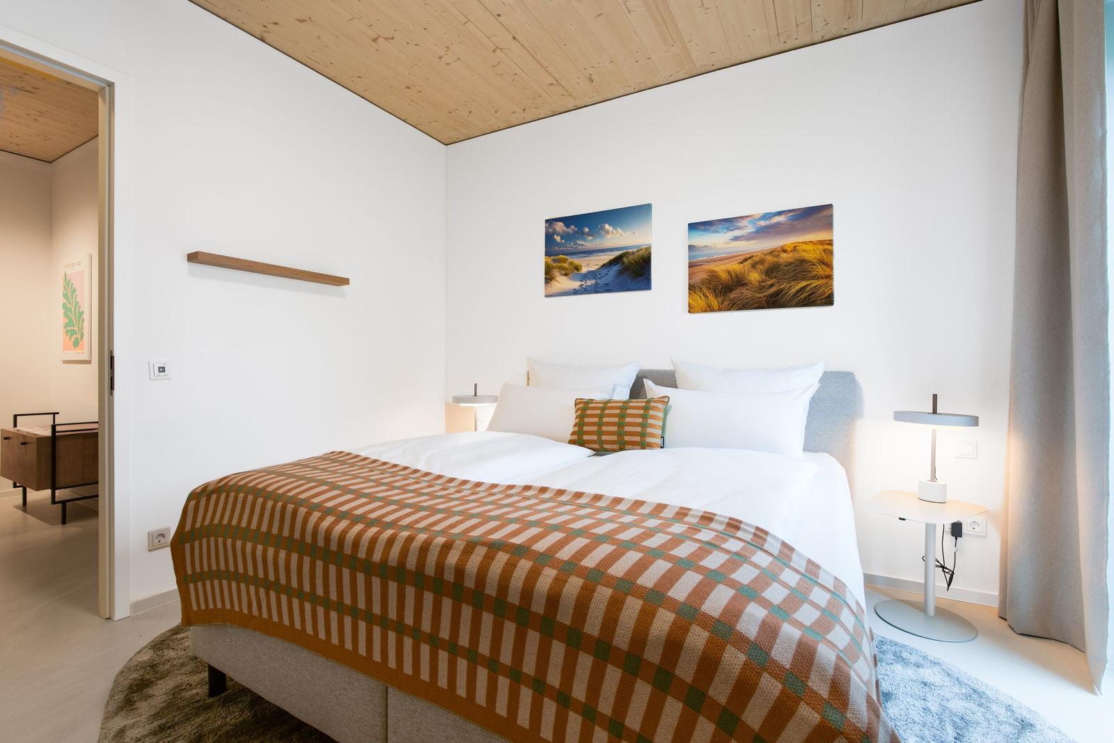 Schlafzimmer mit Bett, zwei Nachttischen und Wandbildern an der Wand.