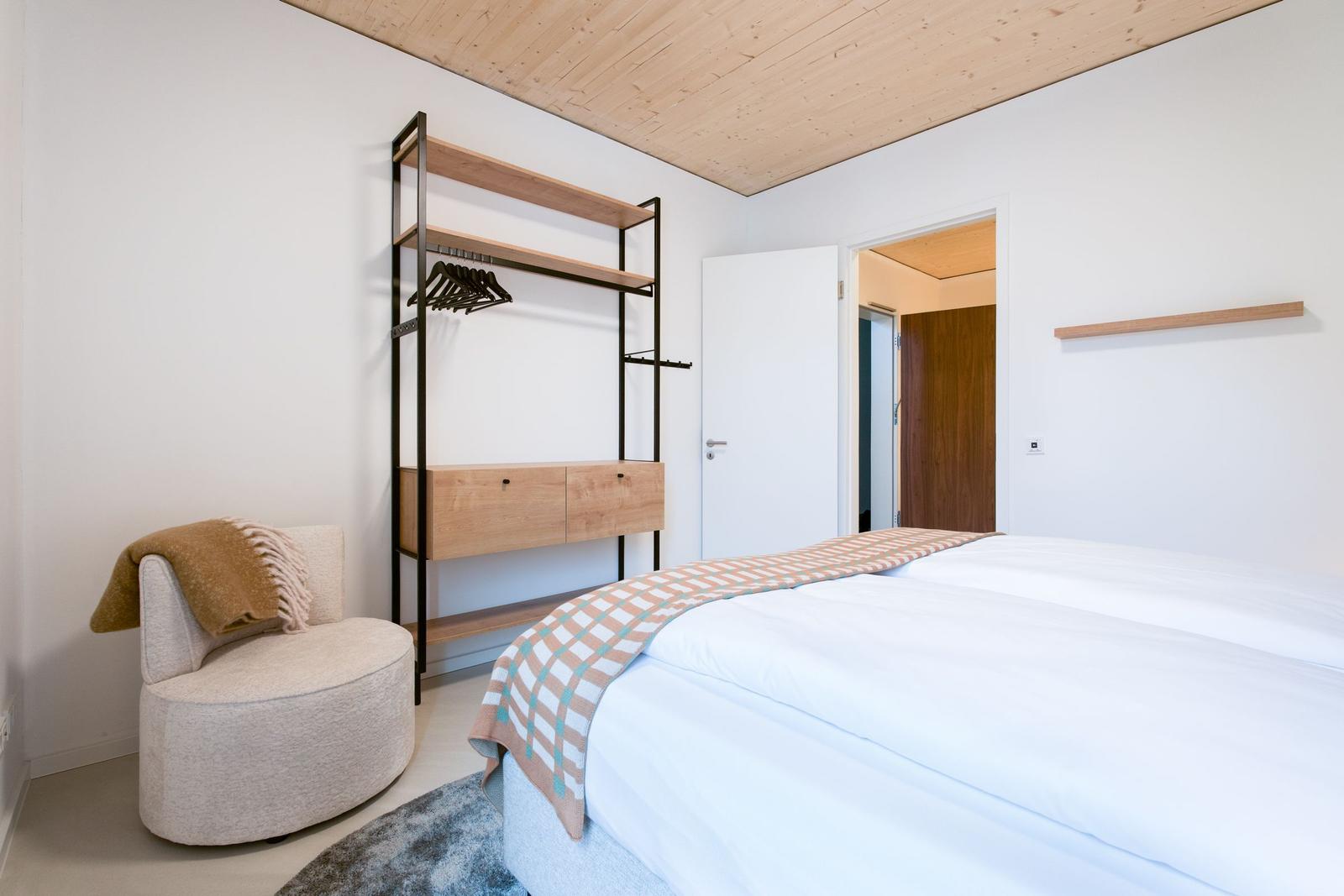 Schlafzimmer mit Bett, Kleiderschrank und Sessel. Holzdecke und weiße Wände.