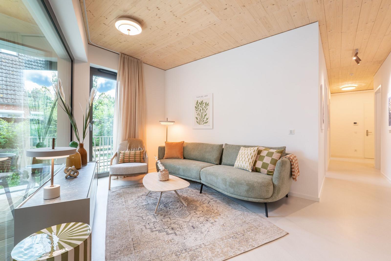 Wohnzimmer mit Sofa, Sessel und Tisch. Holzdecke und große Fenster.