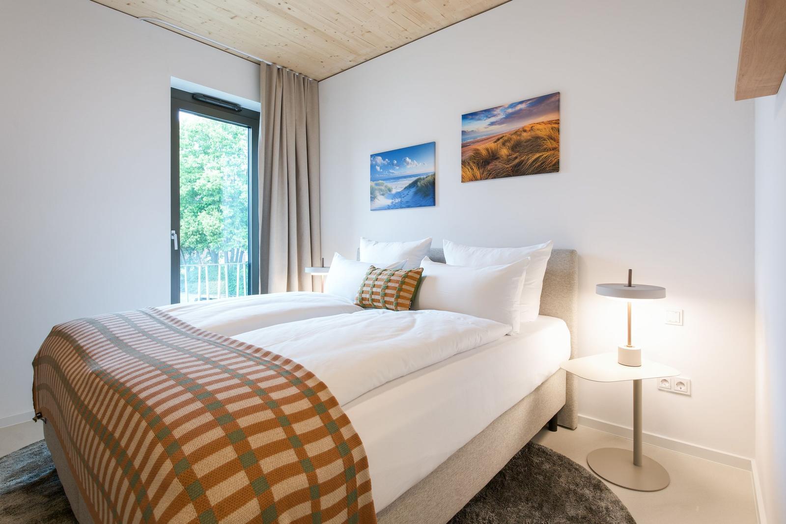 Schlafzimmer mit Doppelbett, Fenster und Wandbildern.
