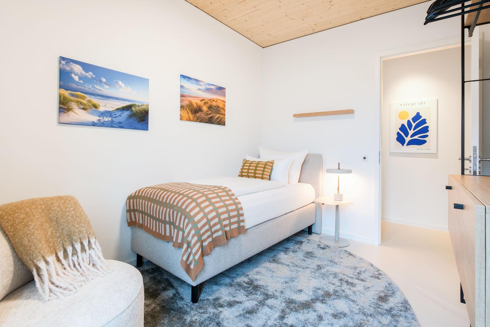 Ein Schlafzimmer mit Bett, Teppich und Wandbildern. Holzdecke und modernes Mobiliar.