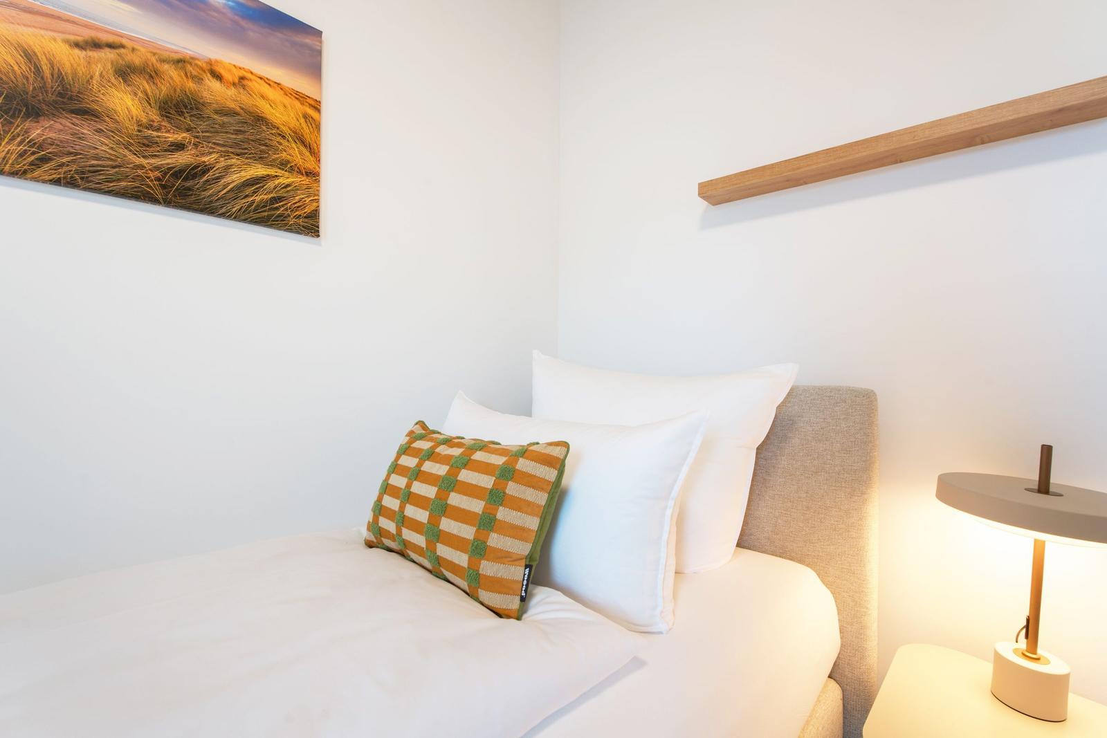 Schlafzimmer mit Bett, Kissen und Wandbild.