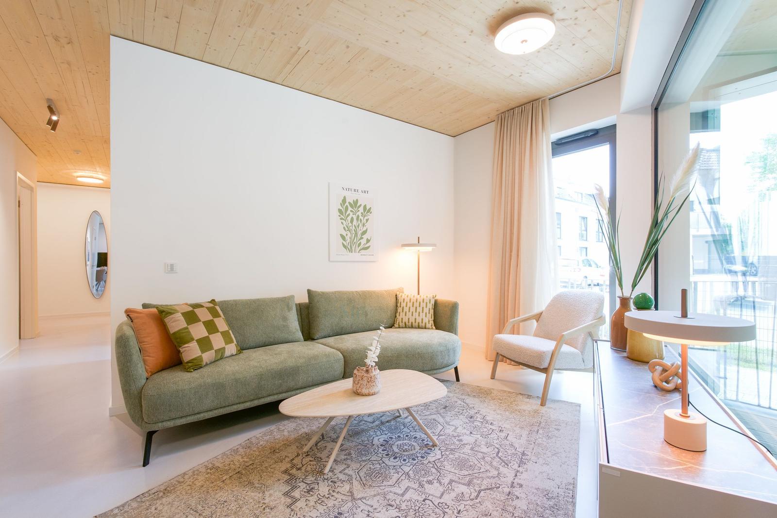 Ein Wohnzimmer mit grünem Sofa, Holzboden und großem Fenster.