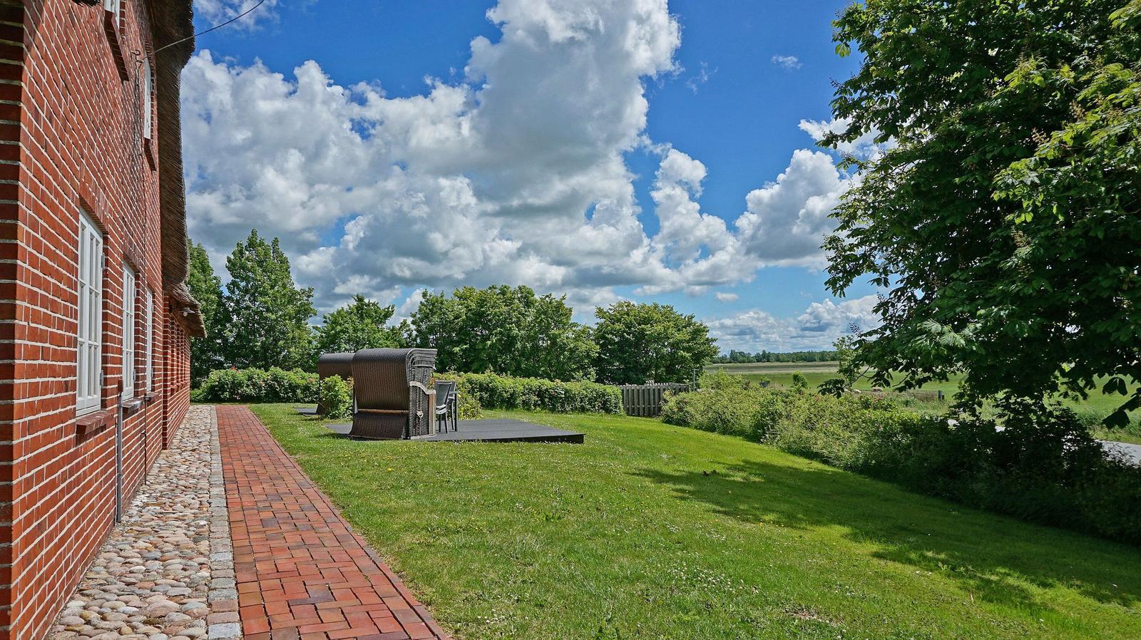 Roter Backsteinbau mit Terrasse, Grasfläche und Blick auf Felder unter blauem Himmel mit Wolken.