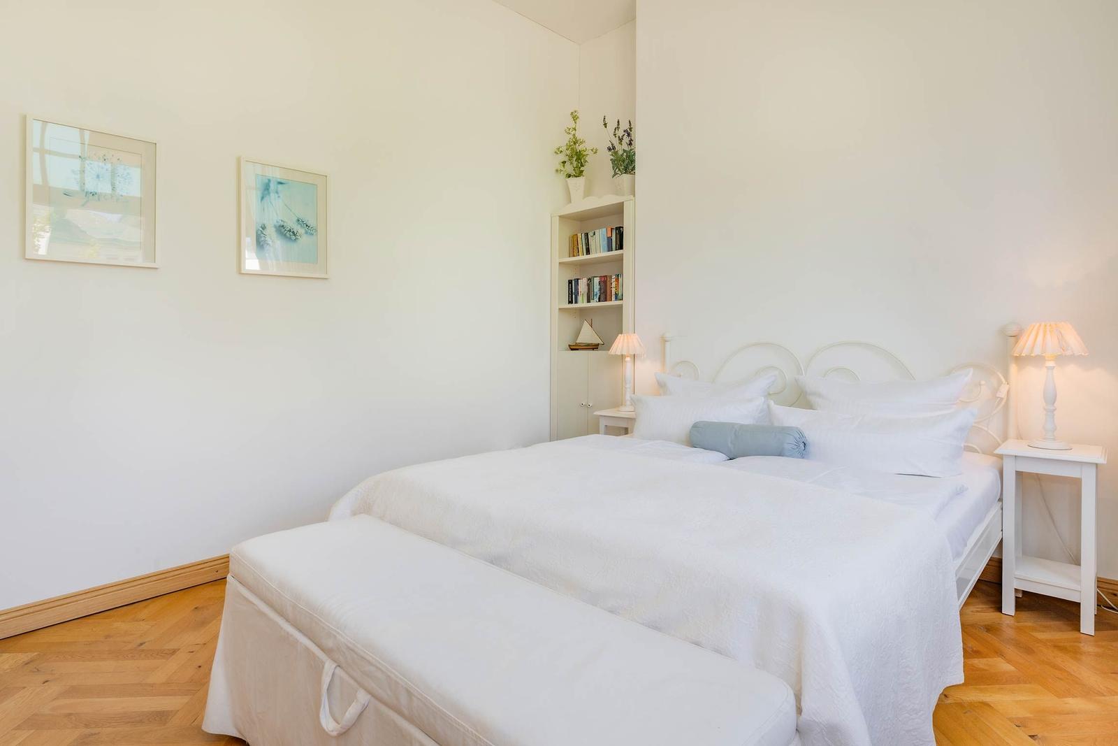 Schlafzimmer mit weißem Bett, Nachttischen und Bücherregal an der Wand.