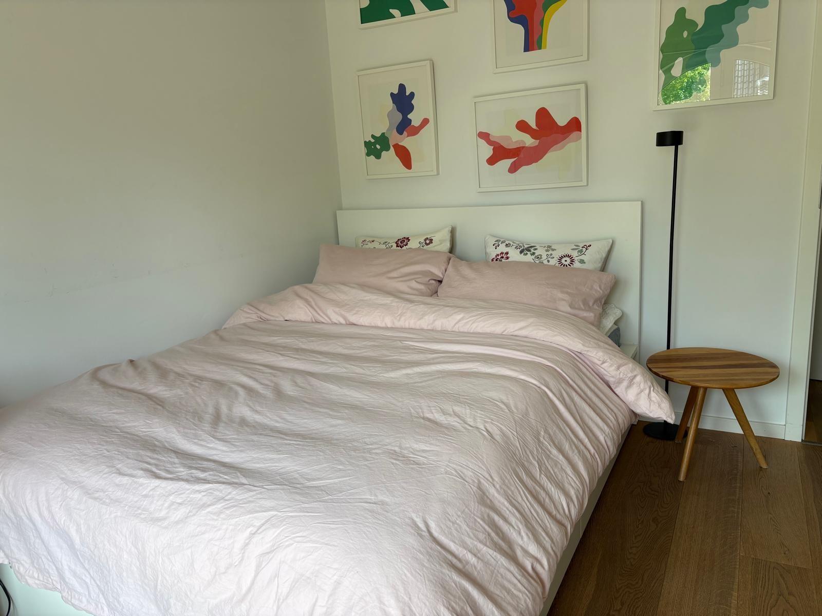 Ein Bett mit rosa Bettwäsche, Wandbilder und einem Holztisch.