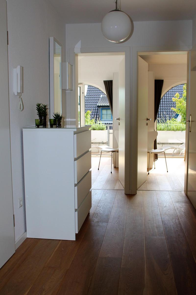 Hallenraum mit Holzboden, weißen Schränken und Blick auf Balkon mit Sitzgelegenheiten.
