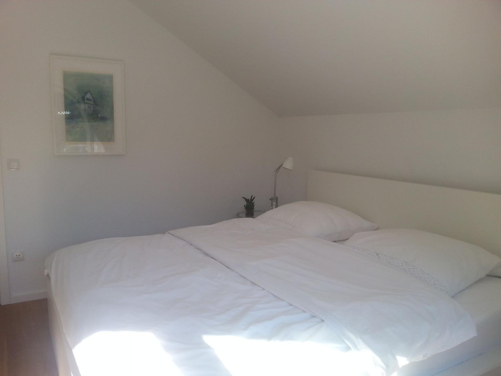 Schlafzimmer mit Doppelbett, Wandbild und Stehlampe unter Dachschräge.