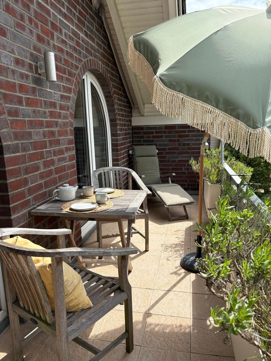 Terrasse mit Tisch, Stühlen, Sonnenschirm und Pflanzen an Backsteinhauswand.