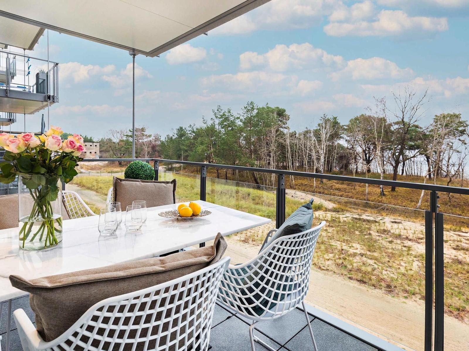 Terrasse mit Tisch, Stühlen und Blumen. Blick auf Wald und Himmel.