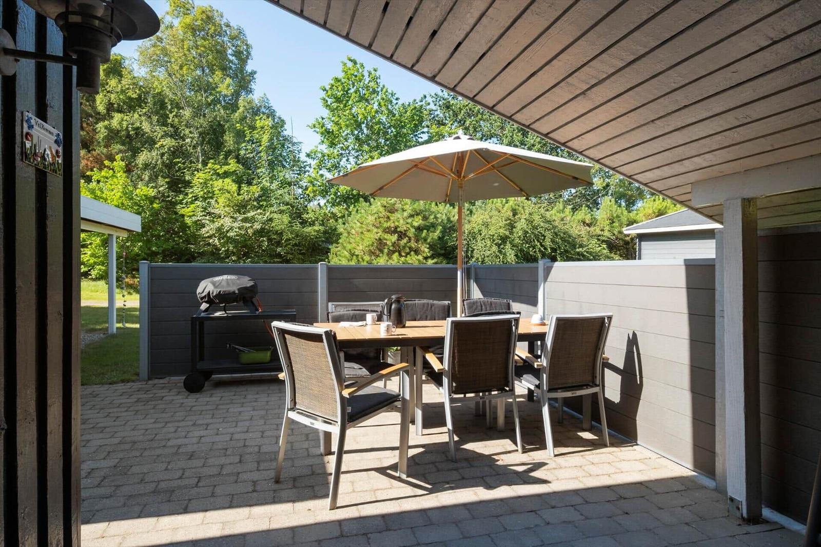 Terrasse mit Tisch, Stühlen und Sonnenschirm. Grill und Zaun sind sichtbar.