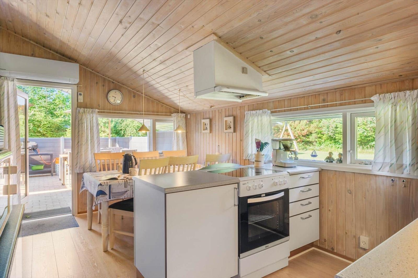 Küche mit Essbereich, Holzwand und -decke, Fenster, Tisch, Stühle und Küchengeräte.