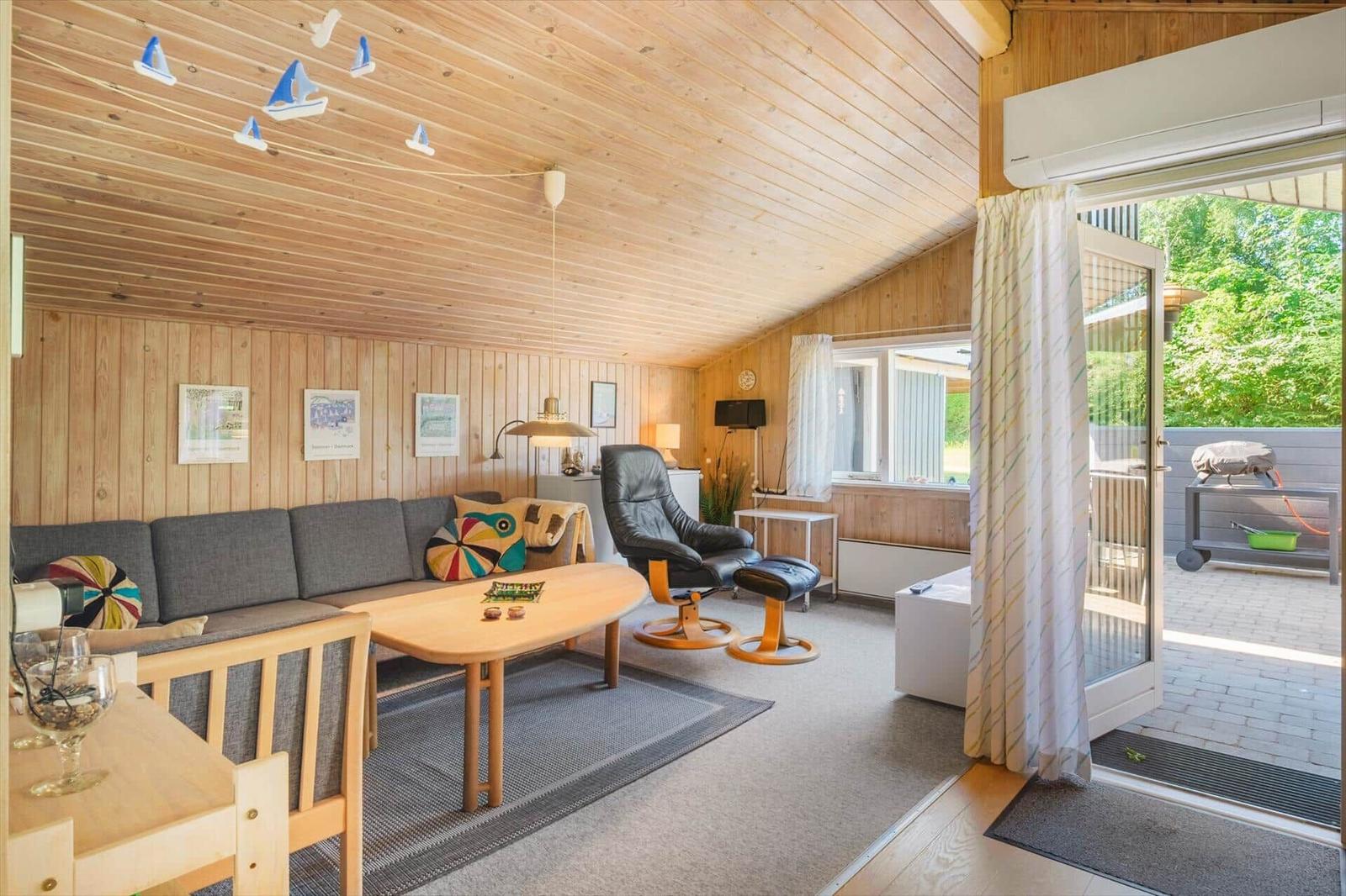Wohnzimmer mit Sofa, Sessel und Terrasse. Holzwände und Decke.