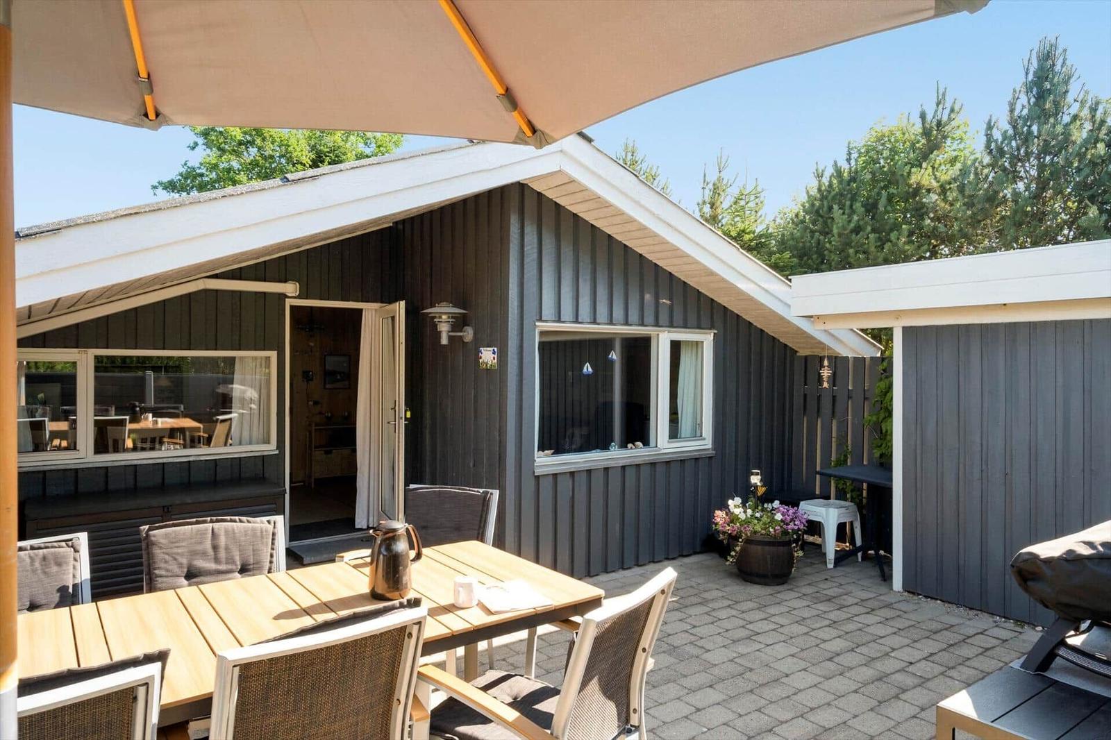 Terrasse mit Tisch, Stühlen und Sonnenschutz vor einem Haus mit Holzfassade.