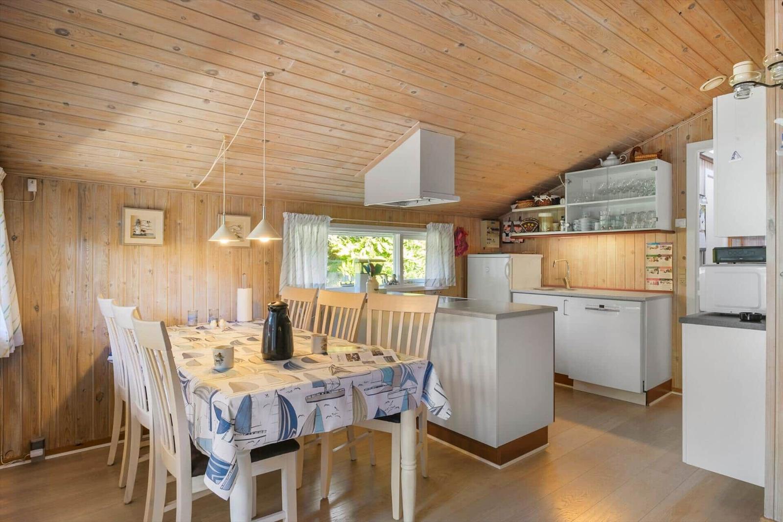 Küche mit Esstisch, Holzwand und -decke, weißer Küchenzeile und Fenster mit Blick auf Grün.