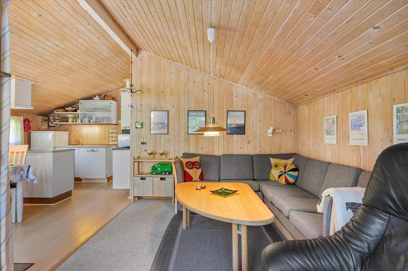 Wohnbereich mit Sofa, Tisch und Küchenbereich. Holzwände und -decke.