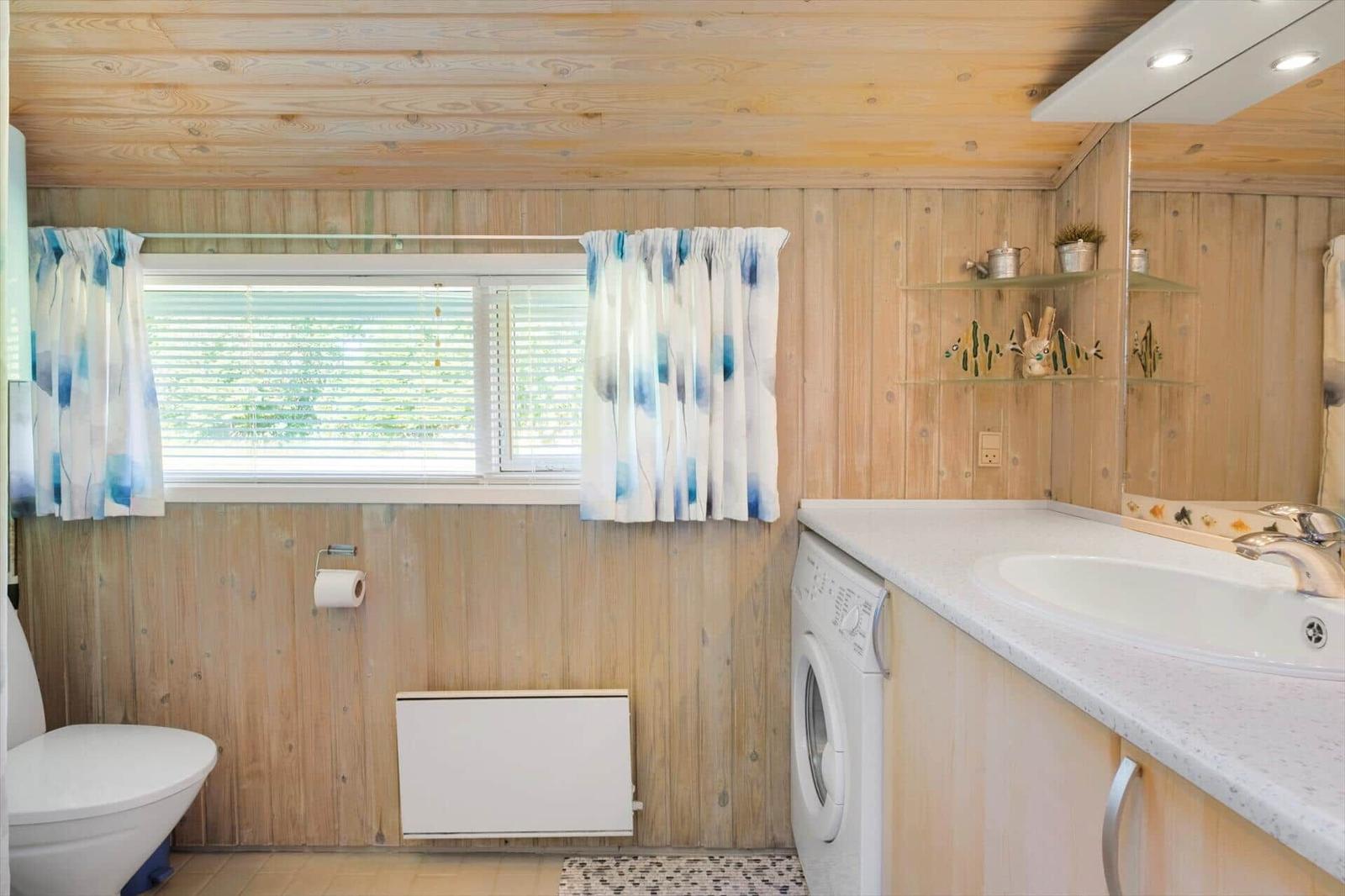 Badezimmer mit Holzwand, Waschmaschine, Waschtisch und Fenster mit Vorhängen.