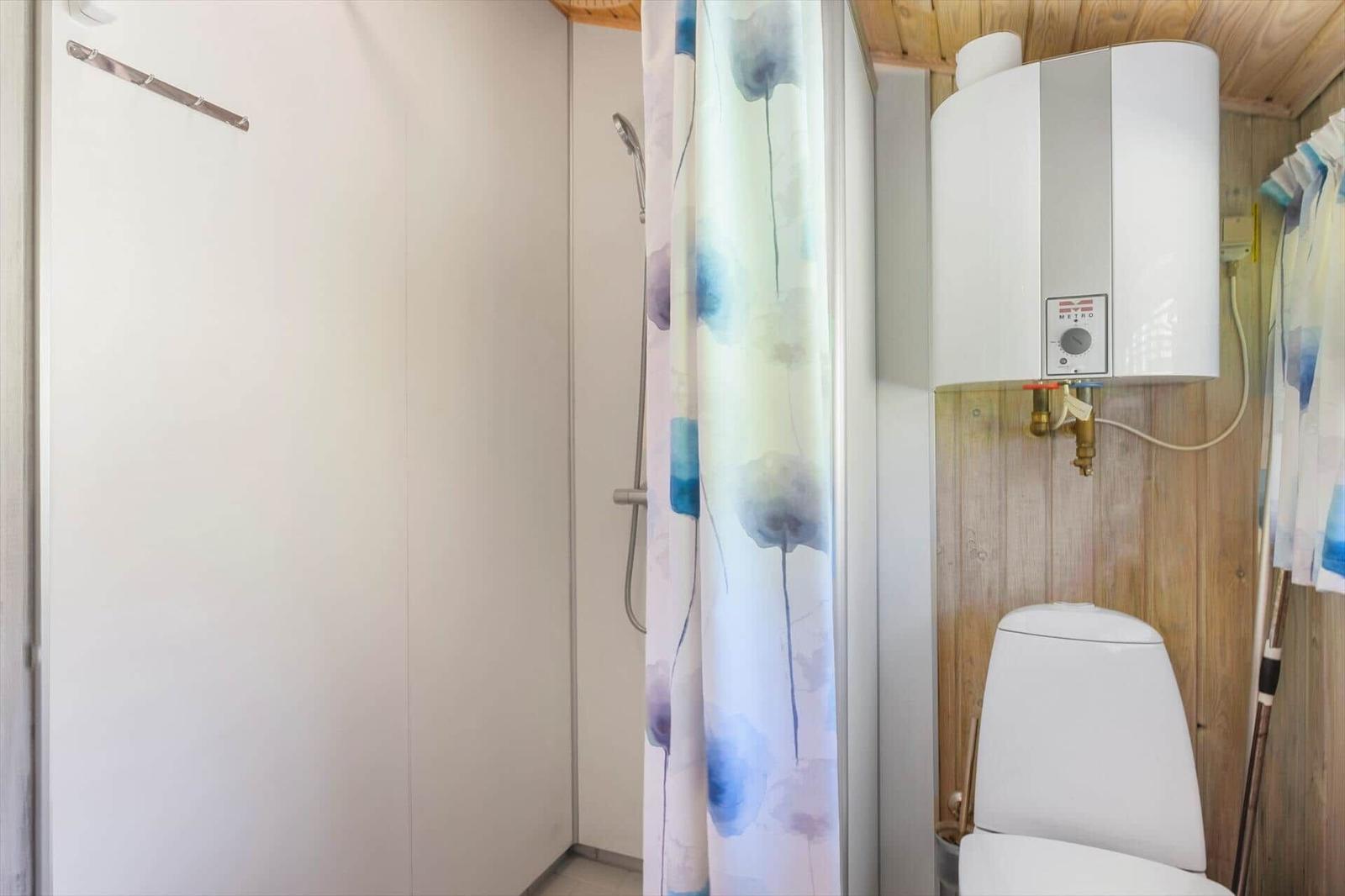 Dusche mit Duschvorhang, Toilette und Wasserheizer an Holzwand