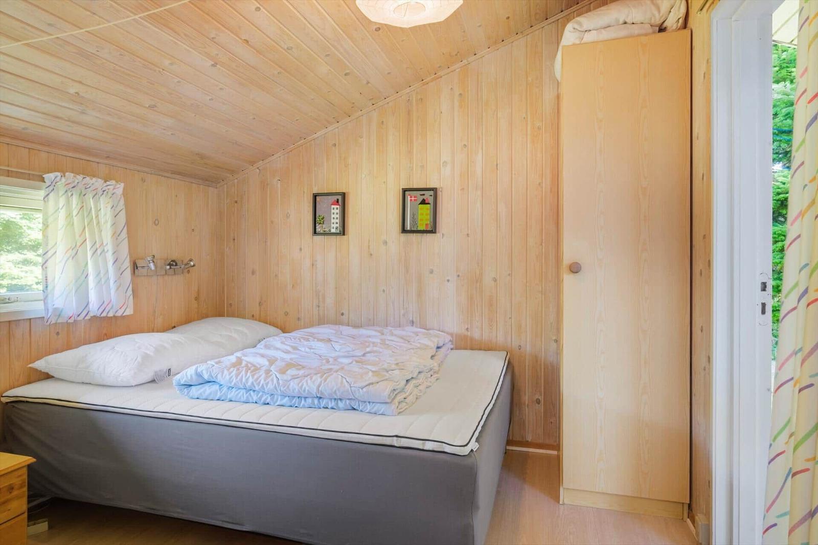 Schlafzimmer mit Holzwand, Bett, Kleiderschrank und Fenster mit Vorhang.