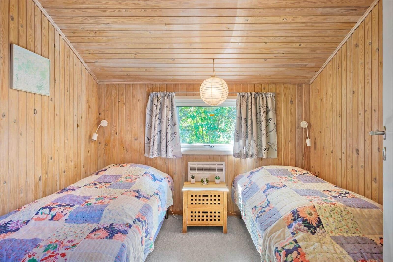 Zwei Betten mit Quilt, Holzwände, Fenster mit Vorhängen und Nachttisch.