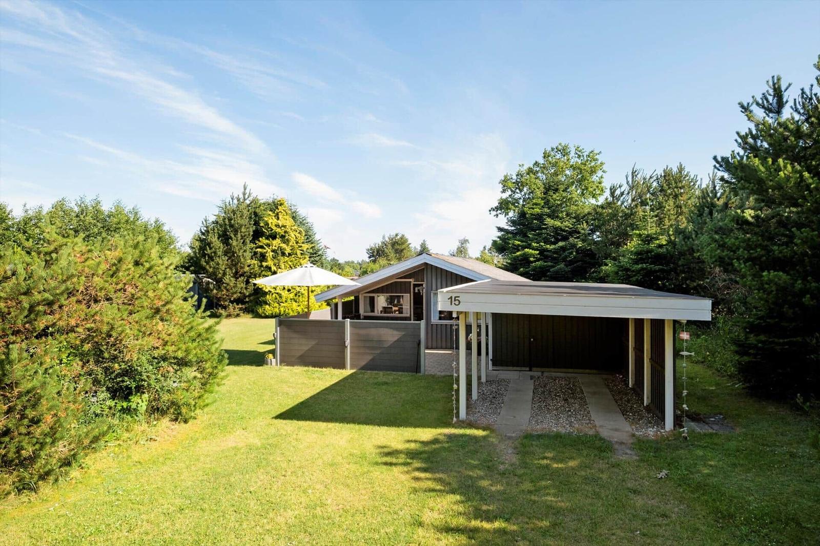Ein Haus mit Carport, Rasen und Bäumen unter blauem Himmel.