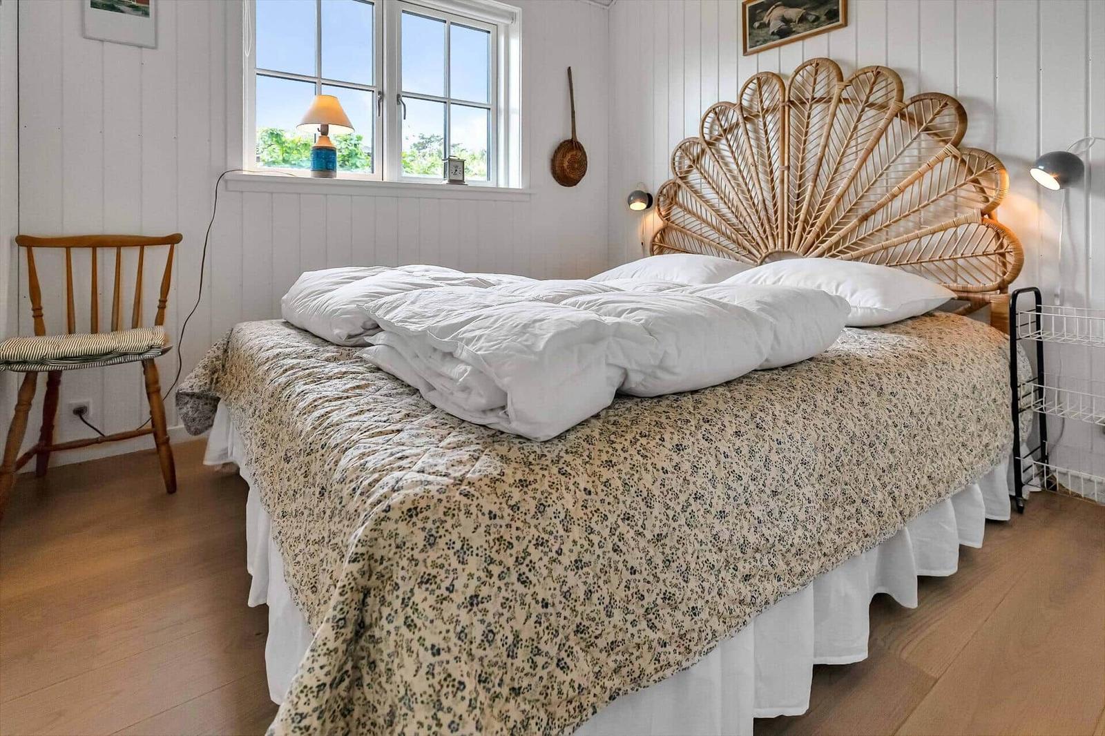 Schlafzimmer mit Bett, Holzstuhl und Fenster mit Blick nach draußen.