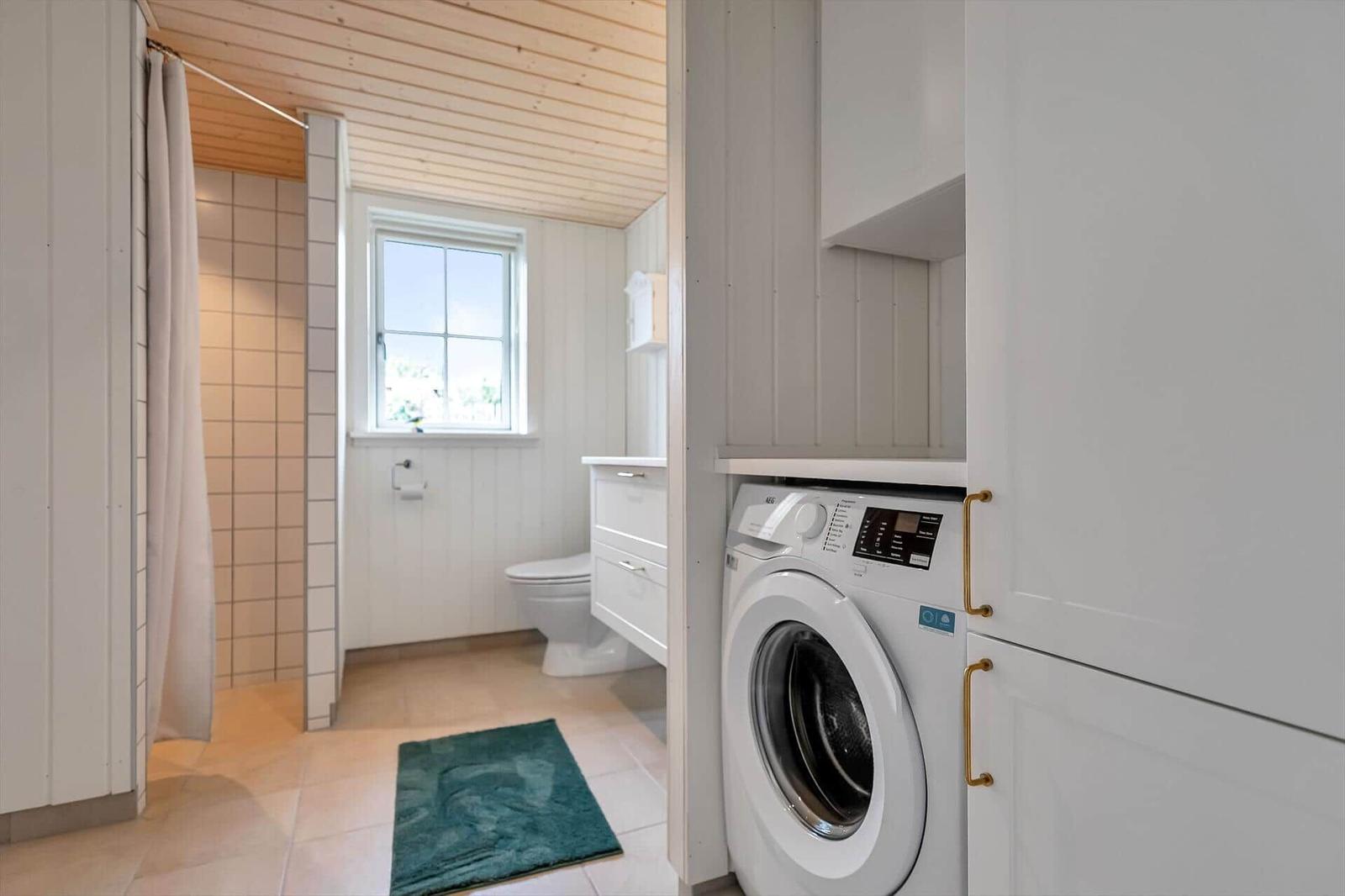 Badezimmer mit Waschmaschine, Toilette und Dusche mit Vorhang.