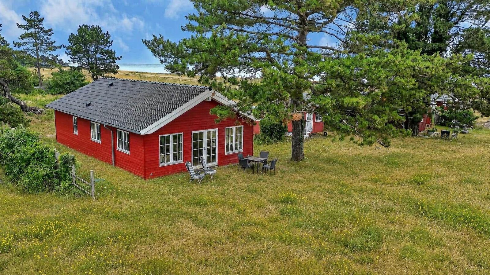 Rotes Ferienhaus mit Terrasse und Garten. Umgeben von Bäumen und Gras.