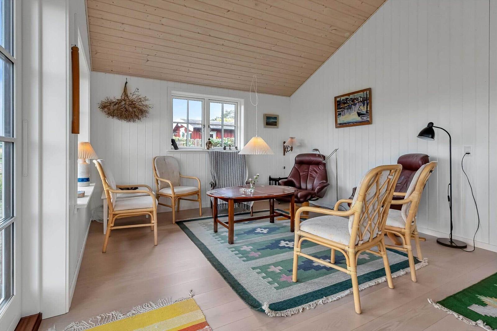 Wohnzimmer mit Holzdecke, weißen Wänden, Sitzmöbeln und Teppich