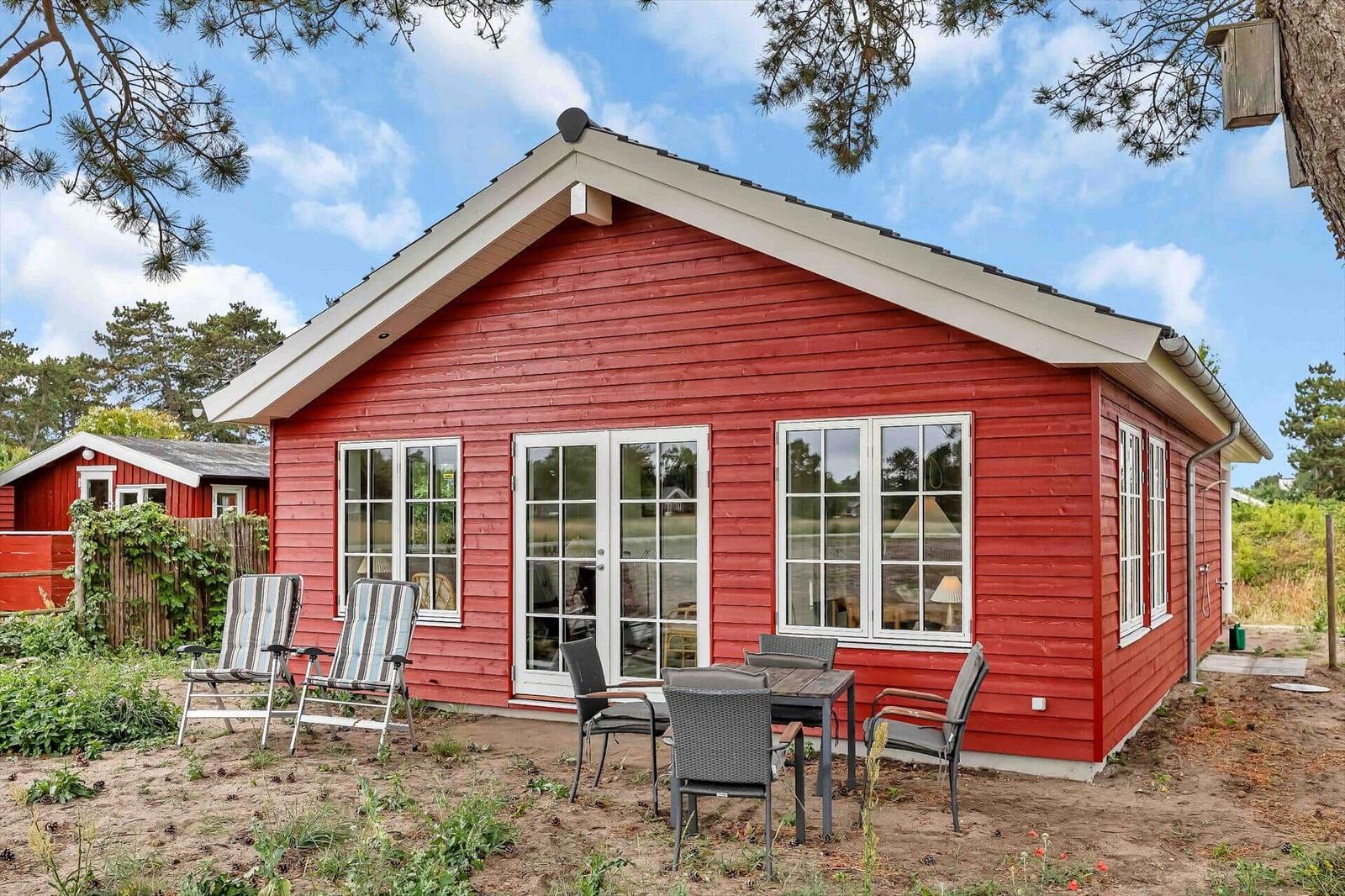 Rotes Holzhaus mit Terrasse und Gartenmöbeln unter Bäumen.