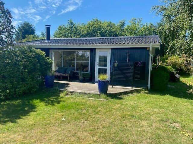A small house with a terrace, glass front, and plants in the garden under a blue sky.